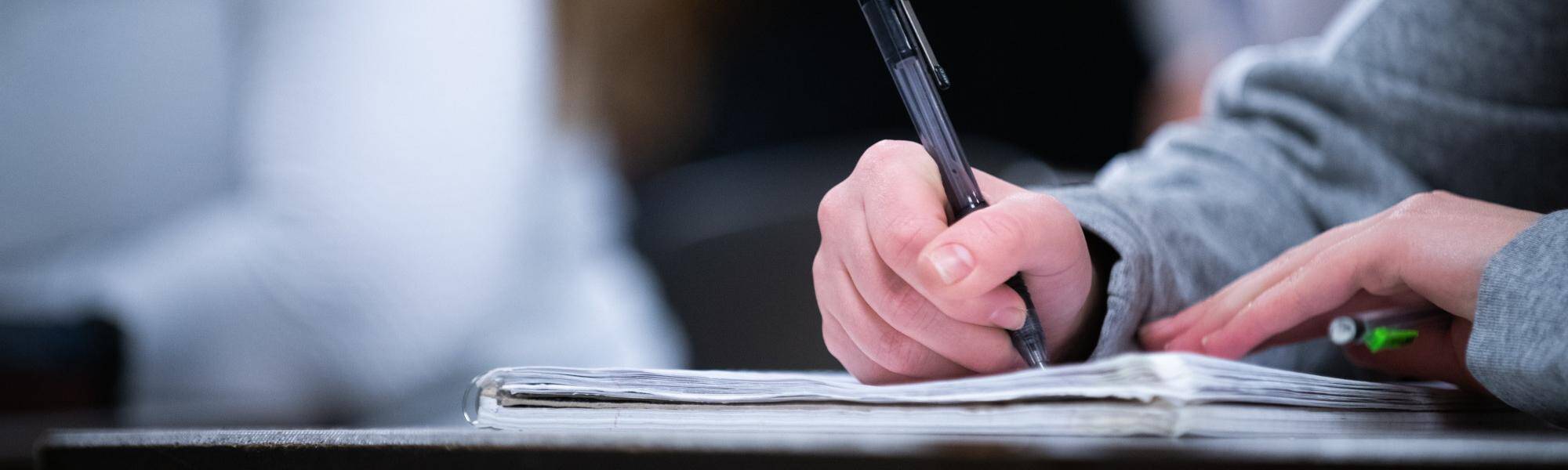 Student hand holding pen and writing on book